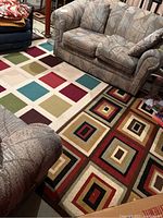 Photo showing two area rugs on floor with sectional couch nearby; geometric patterns with squares and rectangles in multiple colors