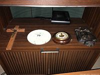 Photo showing a wooden crucifix, a round white dial (likely a thermometer or hygrometer), a round barometer with brass and wood finish, and a dark religious wall plaque.