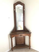 Front view of the wood corner hall table with tall mirror and lower and upper shelves.