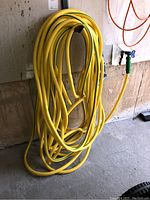 Yellow garden hose coiled and hanging on wall with a green connector on end, showing overall condition and length.