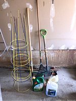 Photo of gardening tools including yellow metal tomato cages, garden rake, garden hoe, containers of weed killer and windshield washer fluid.