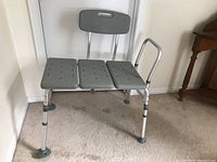 Photo showing the gray plastic shower chair with seat, backrest, and right-side support handle with aluminum frame and rubber tipped legs.