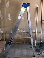 Side angle of the aluminum 5-foot step ladder showing blue top cap and the stabilizer bars between legs.