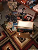 Overview of multiple LP vinyl records laid out on floor beside a brown vinyl carrying case with white interior, showing various album covers.