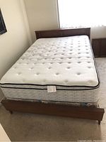 Full view of the double bed setup including wooden footboard, mattress, and box spring on carpeted floor near window.