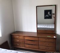 Full view of medium brown wood Mid Century Modern style dresser with nine drawers and rectangular mirror attached, showing overall condition and design.