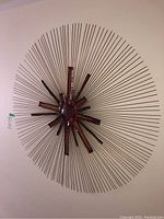 Front view of large circular MCM wall metal art sculpture with radiating thin rods and central copper-toned shapes.