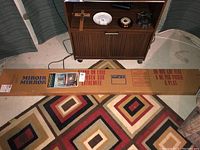 Two long rectangular cardboard boxes containing mirror panels, lying on the floor next to furniture and a rug, clearly labeled MIROIR MIRROR with handling instructions.