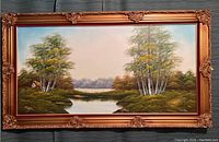 Full view of the framed landscape painting showing the river, trees, and sky with an ornate gold frame.