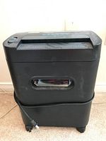 Front view of black shredder showing castors and transparent front window for viewing shredded contents.