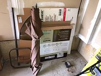 Disassembled patio furniture parts including brown umbrella, metal frame, and cardboard packages in garage.