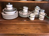 Full set of porcelain dishes including plates, bowls, cups, and saucers arranged on a wooden shelf.
