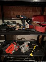 Photo showing all tools on shelving unit including Ryobi drill, Mastercraft screwdriver, Black & Decker sander and saw, hammer, hand saw, toolbox, and tins with drill bits.