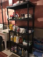 Black 5-tier plastic PVC shelf unit in basement setting with various household products on it (not included in sale).