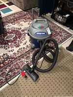 Full view of Shop Vac on carpet with hose and vacuum head attached, showing overall condition and accessories.