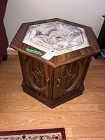Front view of one hexagonal side table showing faux marble inset top and carved doors with brass handles.