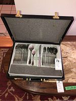 Open black carrying case displaying stainless steel cutlery set arranged inside, including forks, spoons, and knives
