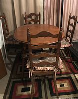 Overall view of wood dining table with four ladder back chairs and chair pads in basement area.