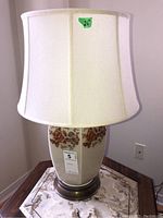 Full view of the 26 inch table lamp showing the fabric lampshade and the floral decorated base standing on a table.