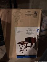 Image of cardboard box showing Mainstays branded 5-piece tray table set with measurements and product illustration.