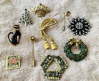 Full view of all 10 assorted pins laid out on fabric, including Christmas pins, stick pins, cat pin, and rhinestone brooch.