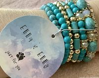 Close-up photo of the set of seven stretch bracelets with attached branding tag reading 'Ella & Elly' and 'just for you'. Bracelets composed of turquoise, gold, and crystal beads.
