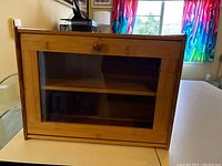 Front view of the bamboo bread box showing the acrylic window on the door and wooden knob.