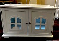 Closed front view of white wooden cat litter box enclosure showing two doors with window cutouts.