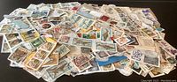 Spread of many international stamps in various sizes and colors laid out on a dark surface showing partial detail of the whole collection.