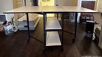 Open table with side panels extended, showing laminated surface, shelves and wheels