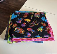 Stack of folded quilting fabric pieces featuring bold colorful cat and bird patterns on black background and striped pink design beneath
