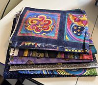 Stack of folded colorful quilting fabric with Laurel Burch designs including sun and moon motifs