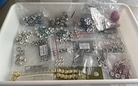Plastic bin with multiple small bags containing various metal, glass, and acrylic beads in silver, gold, blue, purple, and cream colors.