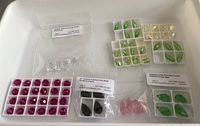 Top view of various crystal beads sorted in trays and zip bags showing different colors and shapes including green, red, pink and clear beads.
