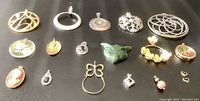 Photo shows 18 assorted pendants and charms arranged on a dark surface including various designs and materials.
