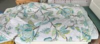 Photo of the queen size quilt showing teal, green, and white floral pattern with branches spread out on a flat surface.