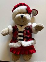 Front view of a Starbucks Bearista Bear plush toy dressed in a red and white Christmas outfit with Santa hat and red plaid jacket, tag attached on ear.