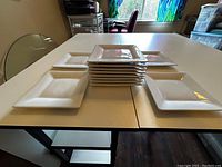 Twelve white square plates stacked and spread on table