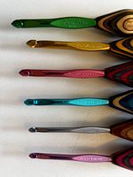 Close-up of six crochet hooks with colorful metal hooks and layered wood handles; visible sizes include 5.5 mm, 6.0 mm