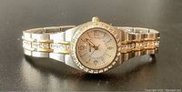 Close up front angle of silver and gold tone plated stainless steel women's watch with crystals on bezel and dial, showing clear details of face and band