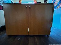 Closed view of the wooden sewing machine cabinet showing two front doors with round metal handles and a smooth wood finish.