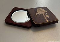 Opened wooden sliding case revealing round makeup mirror inside set into the wood case with the sliding cover partially moved aside.