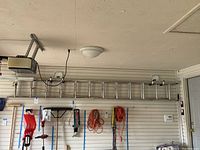 Full side view of the 12 foot aluminum extension ladder mounted horizontally on wall in garage with other tools below.