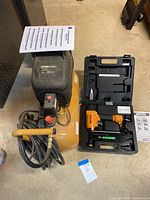 Full view of the Stanley Bostitch air compressor and Bostitch finish nailer in carrying case with tools and manuals.