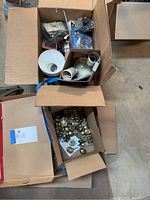 Top view of several open boxes containing cabinet knobs, electrical components including junction boxes and wall plates, and tools.