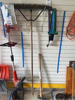 Push broom with rough bristles and wooden handle, 6 pound sledge maul with wooden handle on floor near a wall