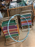 Four metal-frame beach chairs with striped fabric seats and a wooden hanging chair in the background, plus a blue and silver hula hoop leaning against chairs.