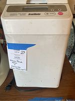 Front view of Hitachi Bread Maker showing white outer case, control panel on top with buttons, some surface dirt and wear.