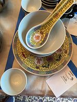 Soup bowl with ceramic spoon resting inside, showing the multicolor detailed pattern with red stylized symbols on the spoon and bowl rim in yellow color with floral elements