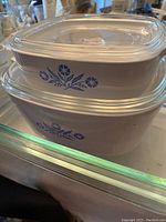 Stacked blue and white Corningware casseroles with floral patterns and clear lids